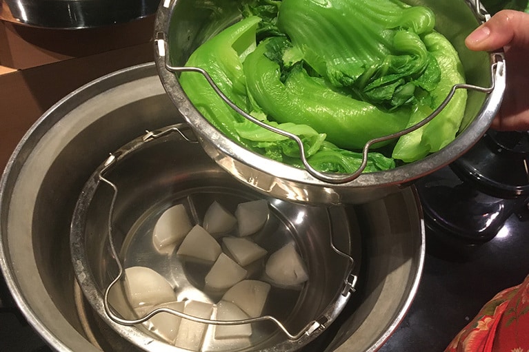 電鍋の便利なポイントの1つは、2つのものを同時に調理できること。大根と、最後に添えるからし菜を同時に下茹で可能。大根が入っている器に大根がひたるくらいの水を入れ、 二段重ねで電鍋にセットして、外鍋に水1カップを入れてスイッチをオン。スイッチが上がったら調理完了。同時調理用の器がない場合は、深めのお皿の上にお箸をおいて、その上にもう1つのお皿を重ねればOK。