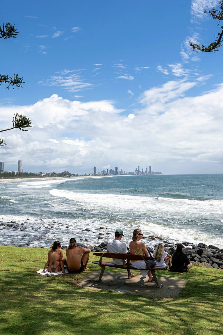 のどかな海辺の公園。くつろぎながらサーファーを眺める人たちがいっぱい。