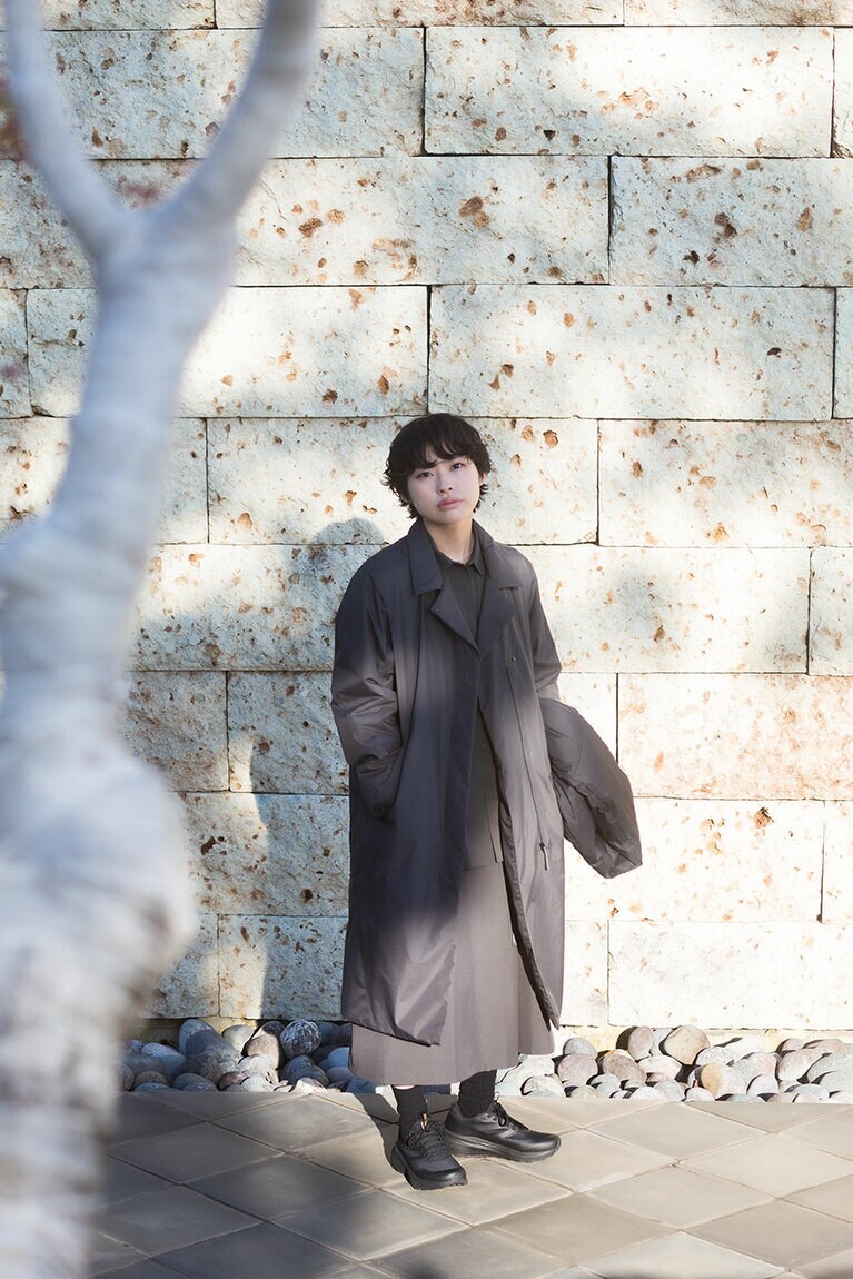 一枚一枚表情が異なる大谷石で作られたギャラリーの壁の前で。ダウンスカーフ 42,900円