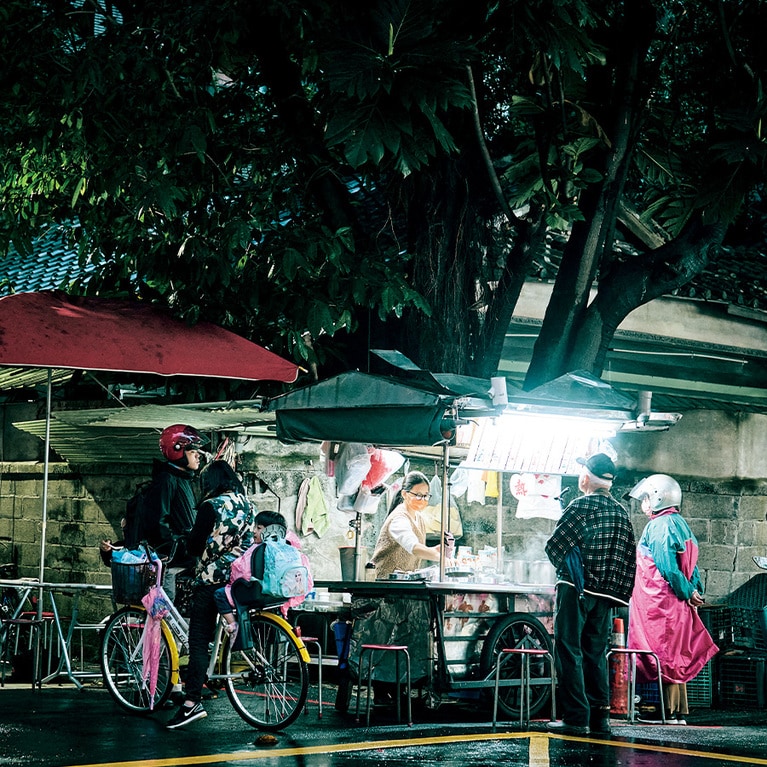 夕方になると、大きな木の下にどこからともなく現れる荷車。小雨がぱらつく中、住宅街にポツンと佇む静かな屋台には、バイクや自転車で次々に人が集まり、あっという間に行列が……。