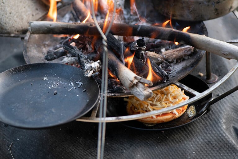 焚き火台と地面の隙間にピザを入れて焼く。写真の焚き火台は、タキビズム リアル ファイヤースタンド ジカビ Mサイズ 17,600円／UPI