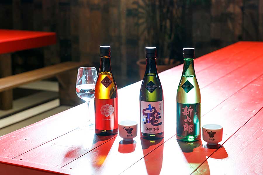 杉能舎を代表する日本酒を、昔ながらの酒蔵の中で試飲。左から：ワイングラスで味わいたい純米吟醸「フキノホマレ」、純吟生搾り「和膳会釈」、辛口の純米吟醸「新九郎」。