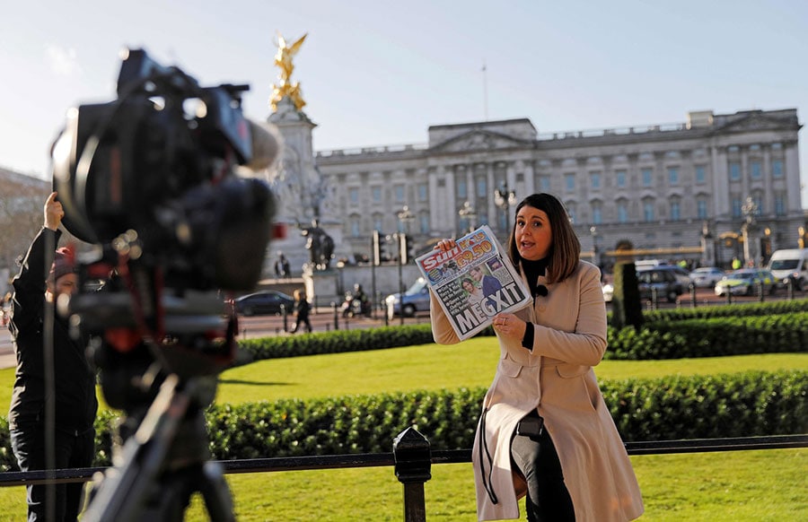 1月9日、メーガン妃夫妻の英王室引退「MEGXIT」の見出しが躍る英国大衆紙「サン」を手に、バッキンガム宮殿前から中継するテレビリポーター ©アフロ