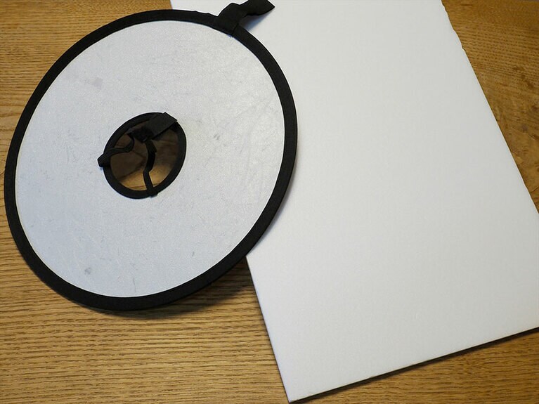 左は真ん中にレンズを通して使用する市販の折りたたみ式レフ。右の100円ショップなどで売られている白いボードもレフ版になる。