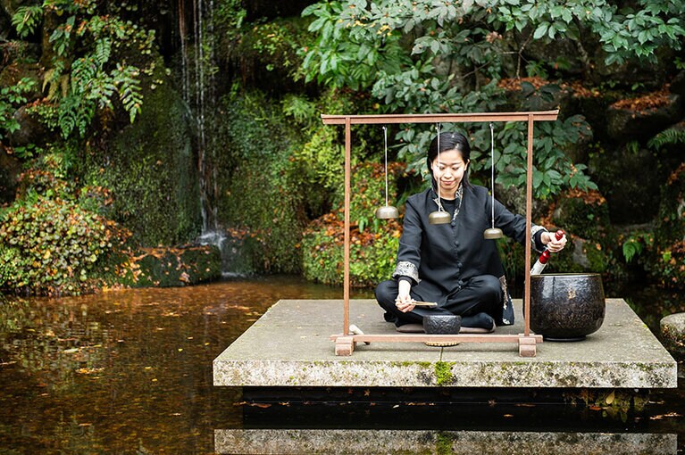 滝をバックにウェルカムミュージックでお出迎え。楽器は、仏具をアレンジしたオリジナル。