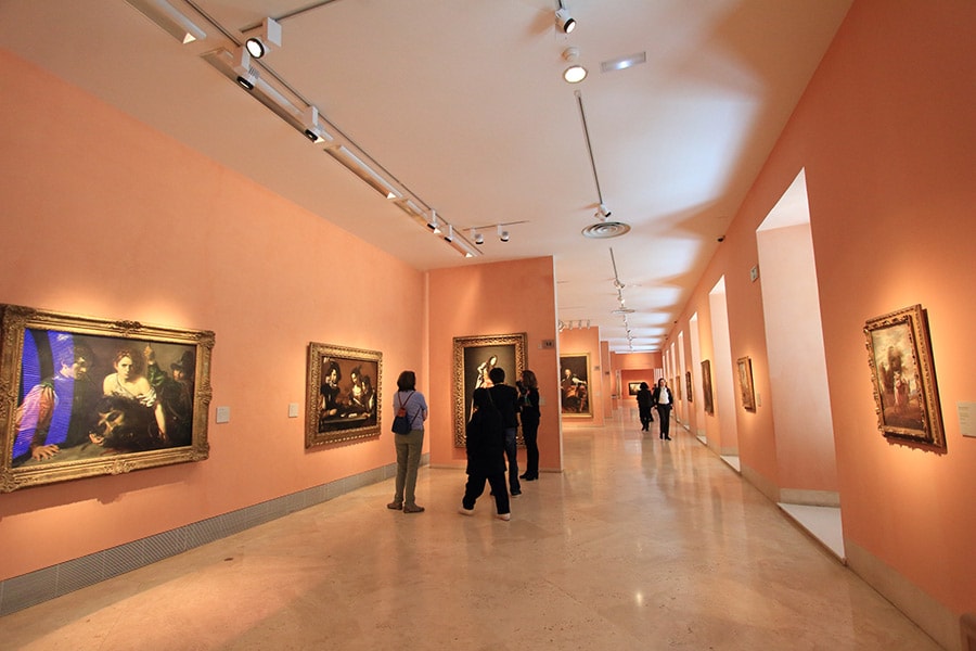 美術館外観の色と同系色の、淡いオレンジの壁に絵画が飾られている。