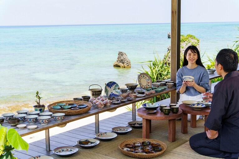 海辺で器を手に取り会話を楽しむ。