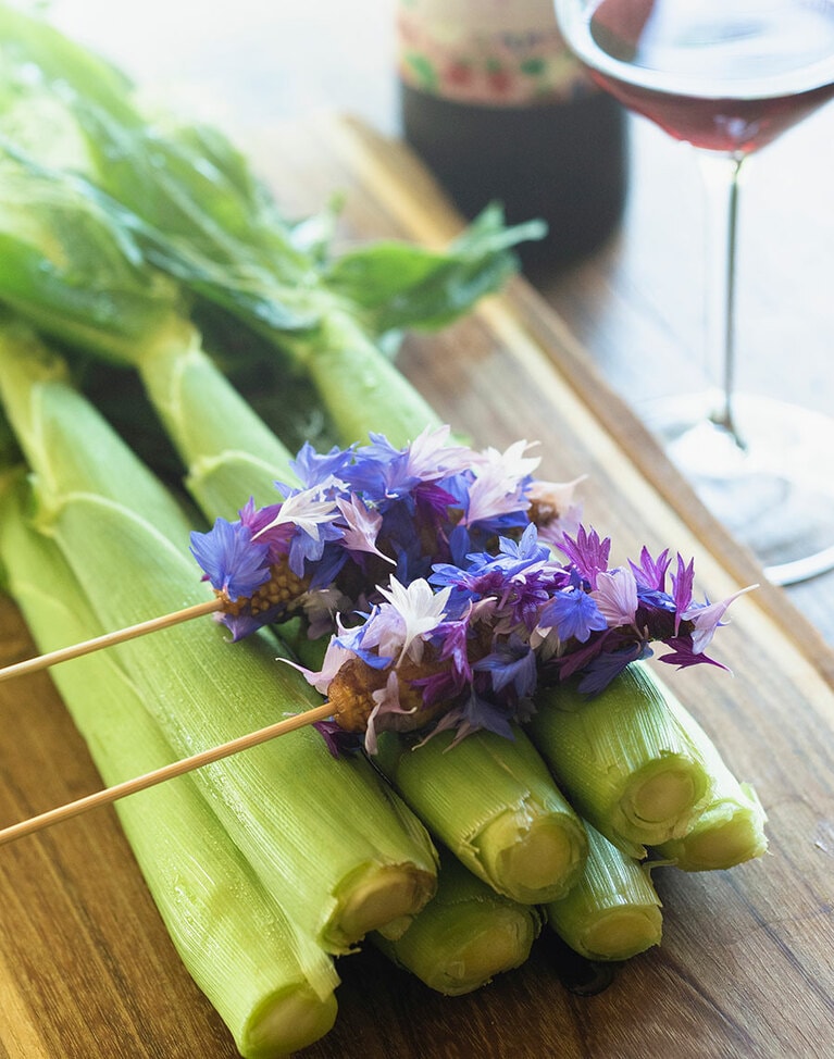 串に刺したベビーコーンに、甘辛い味付けをした猪のベーコンを巻いてコーンフラワーを纏わせた“夜店”。