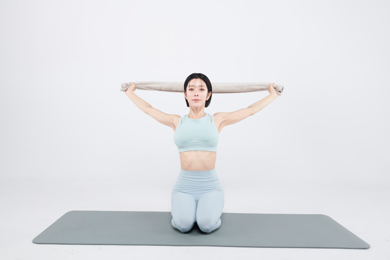 【STEP.3】5秒ほどかけて息を丁寧に吐く。タオルを軽く外側に引き合って5秒キープ。鎖骨が後ろに回って胸が自然に開く感覚で