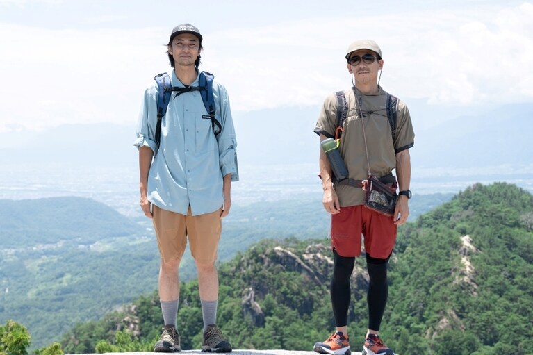 猪野正哉さん（左）と田中行太さん（右）＜猪野＞ロングスリーブシャツ 14,850円、ソフトシェルショーツ 10,450円、キャップ 4,290円、トレッキングシューズ 13,970円すべて／コロンビア（コロンビアスポーツウェアジャパン）＜田中＞ジャケット 49,500円、Tシャツ 35,200円、ショーツ 22,000円、キャップ 13,200円、ザック 46,200円、サコッシュ 8,800円／全てクレッタルムーセン（スプートニク）、シューズ 24,200円／ブルックス（アキレスお客様相談室）。