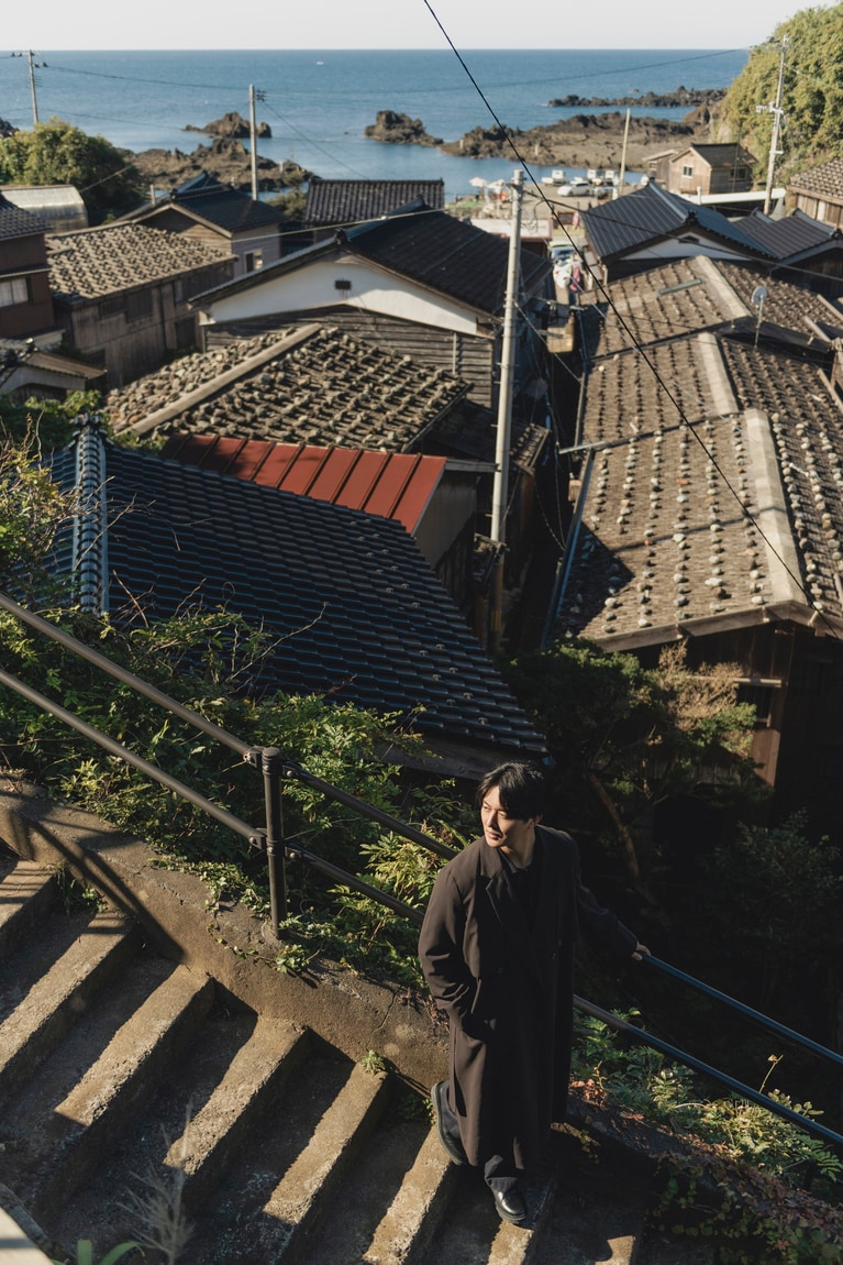 高台から小木海岸と集落を望む。屋根の上に石が置かれた「石置木羽葺屋根」のようすもよく見える。