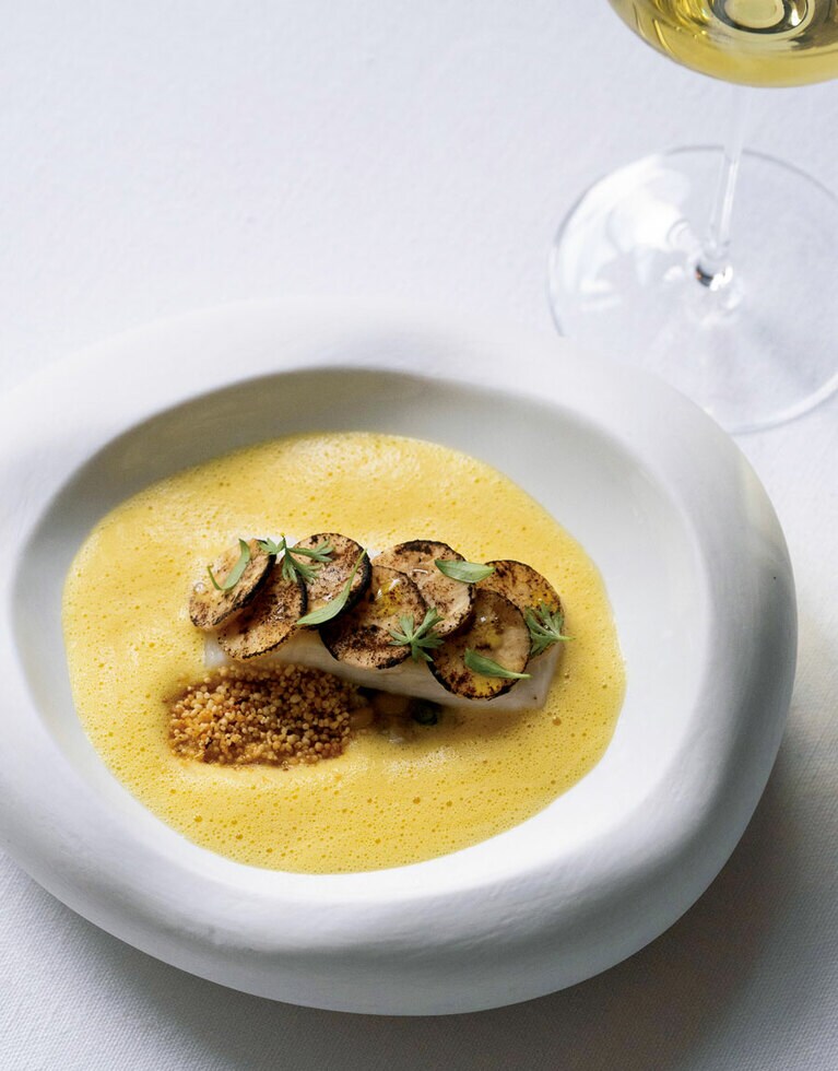 ブラジルの郷土食ムケッカを再構築した魚料理。赤いヤシ油がココナッツと混ざり美しい黄金色に。トーストしたキャッサバのクランブルを添えて。