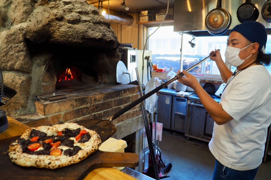 ピザを焼く吉岡知弘店長。ピザ窯は房州石を使ったオリジナルのもの。