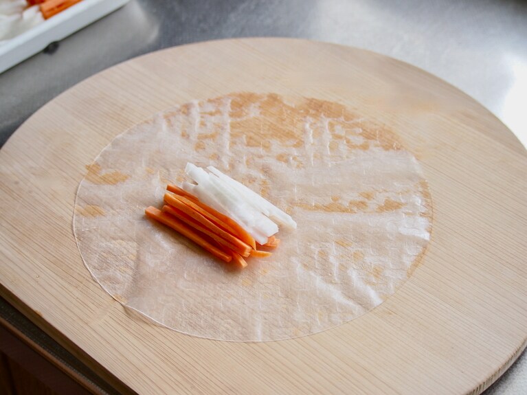生春巻きの皮を水で濡らし、まな板の上に置く。中心より少し手前に大根と人参を並べてのせる。