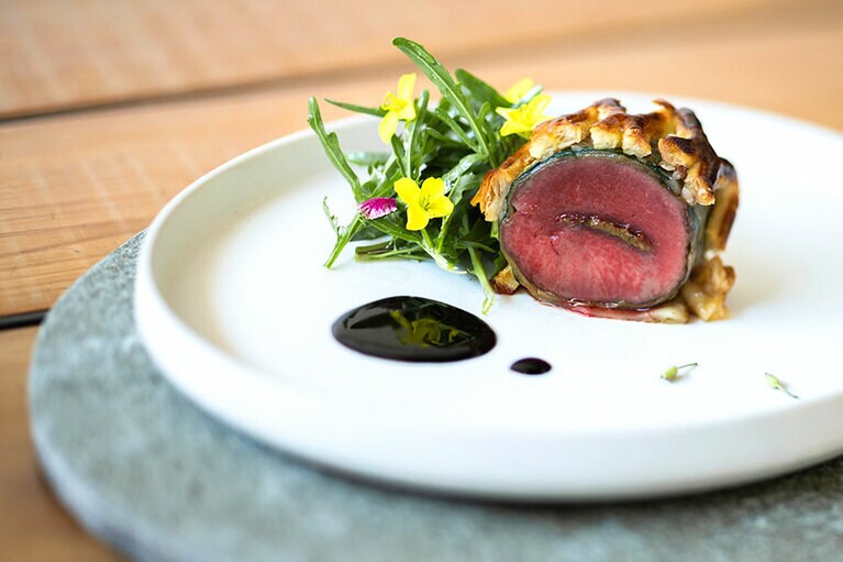 “鹿もも肉のウェリントン”。野生のセルバチコと花を添えて。肉の中心には自家製の蕗味噌。煮詰めた白樺の樹液を加えた赤ワインソースでいただく。