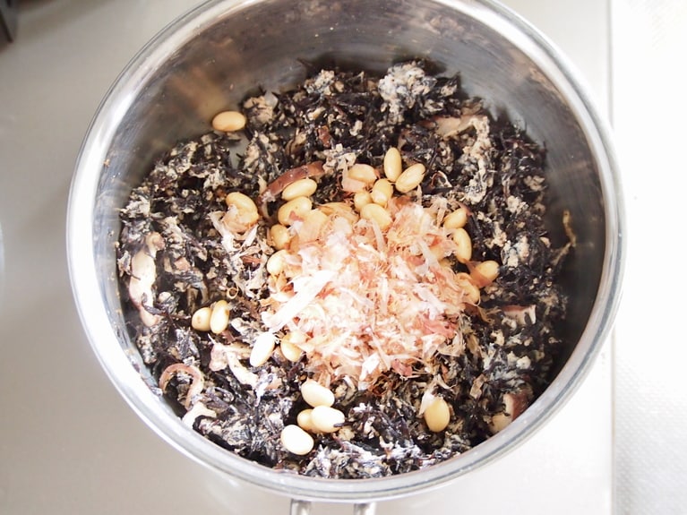 鶏肉の赤みがなくなってきたら、大豆水煮缶、鰹節を入れる。椎茸のもどし汁、水を適量加え、焦げ付かないように弱火で煮込む。