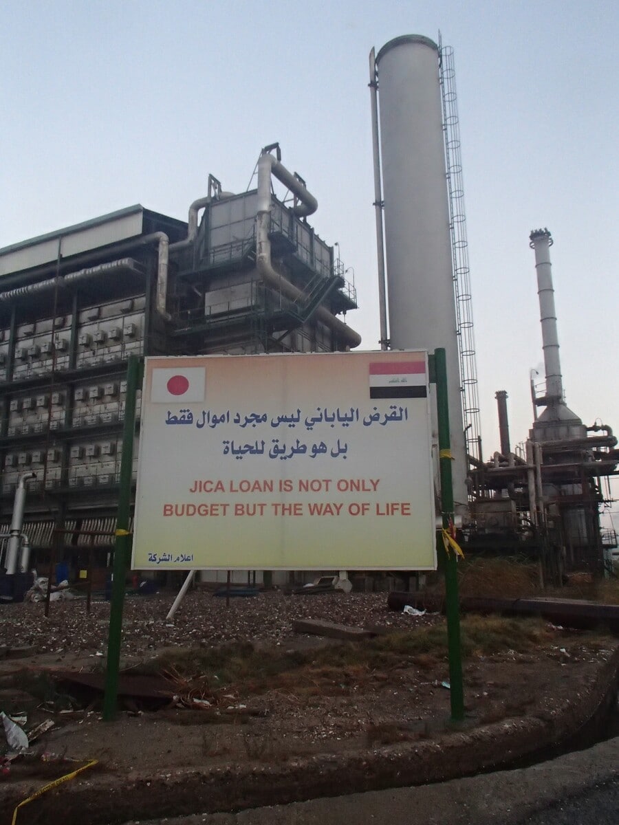 イラク駐在時代の写真。看板には「JICAの資金は単なるお金にあらず、我々の生活につながっている」というイラク側が発案したメッセージが。