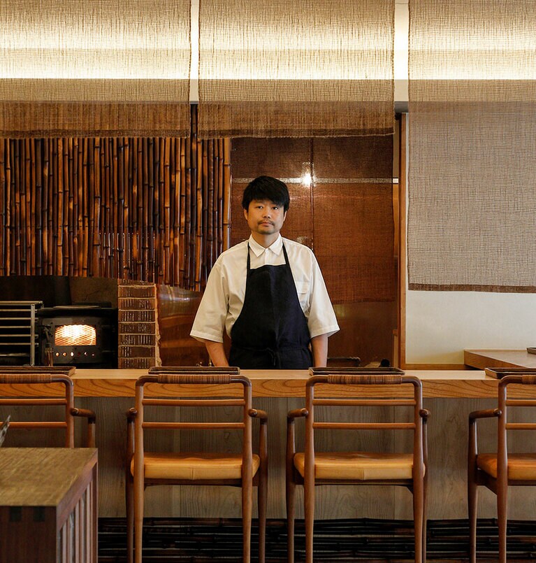 店主の吉岡幸宣さん。右奥に薪火の窯が見える。