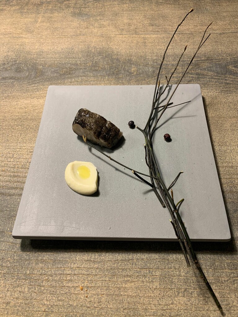 真鱈は、イカ墨を使った富山の塩辛「イカの黒づくり」を塗って熟成させて熾火で焼く。添えられているのはカリフラワーのソース。右側に置かれているのは敷地内に生育しているクロモジの枝。ほのかな香りを楽しみながら真鱈をいただくのだ。