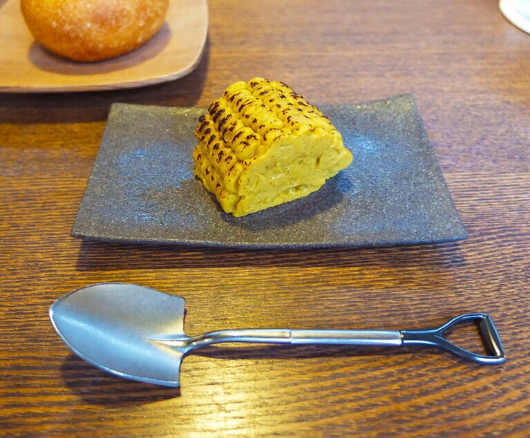 ［SHÓKUDŌ YArn］「あれ？」と思いながらシャベルのスプーンで口にした瞬間、誰もが笑顔になれる一皿。「炭火焼き朝採りトウモロコシ」。