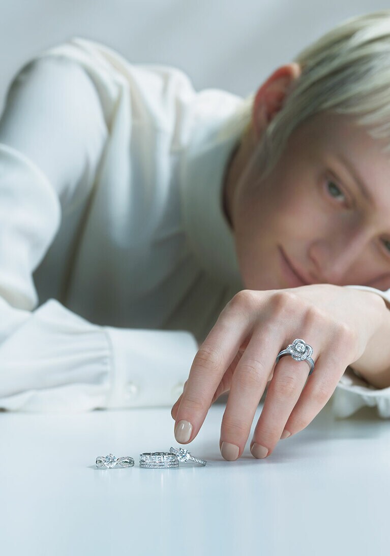 リング：〈薬指〉「ピヴォワンヌ」ソリテール（WG×センターDIA0.2ct～）814,000円～、〈テーブル上・右から〉「ビーラブド」ソリテール（PT×センターDIA0.2ct～）561,000円～、「キャトル ラディアント」（WG×DIA）2,706,000円、「ポン ドゥ パリ」ソリテール（PT×センターDIA0.3ct～）836,000円～（すべて予定価格）／すべてブシュロン（ブシュロン クライアントサービス）　ブラウス／エディター私物