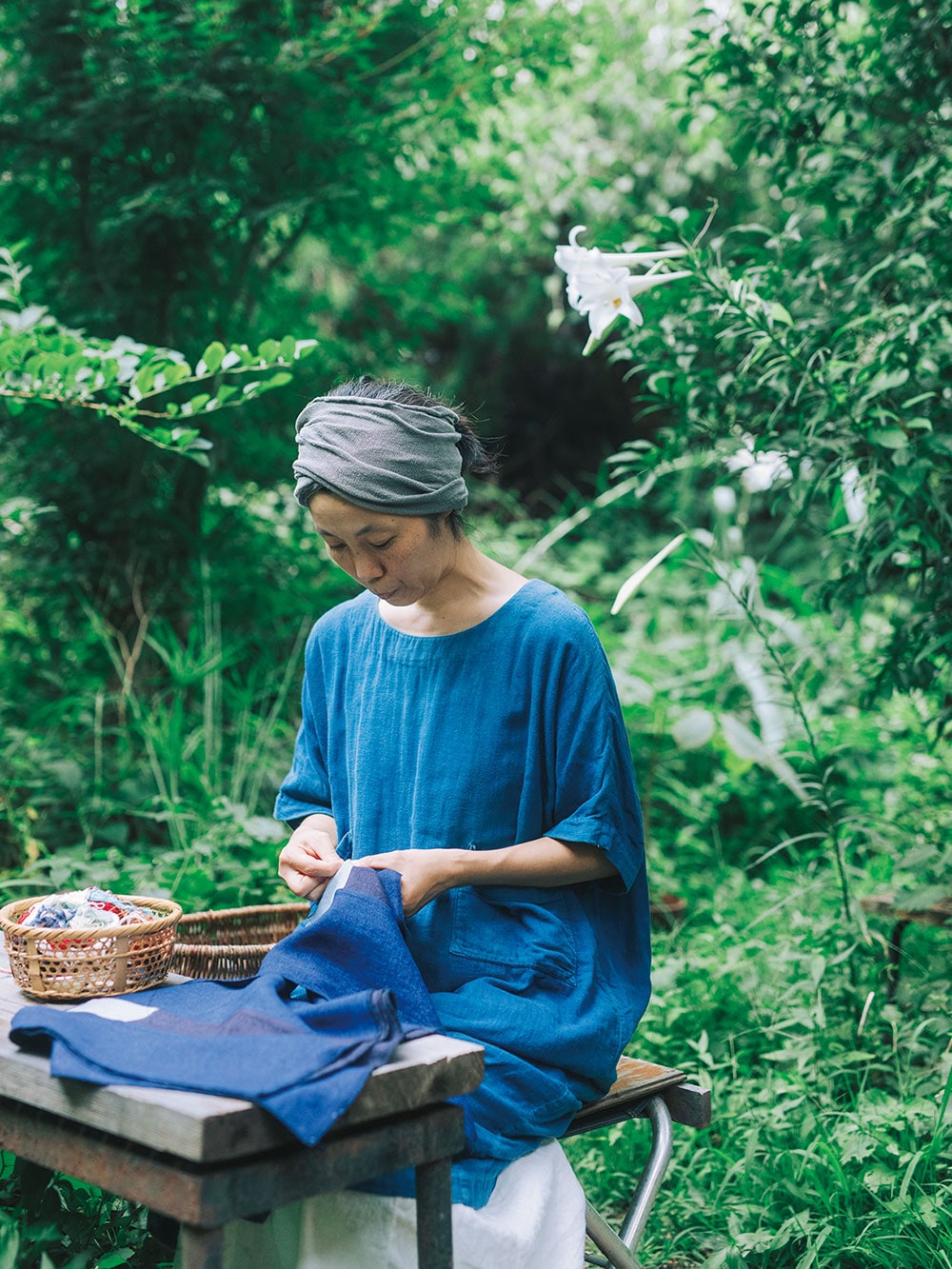 鈴木智子さん。草花が生い茂る庭で縫い物を。