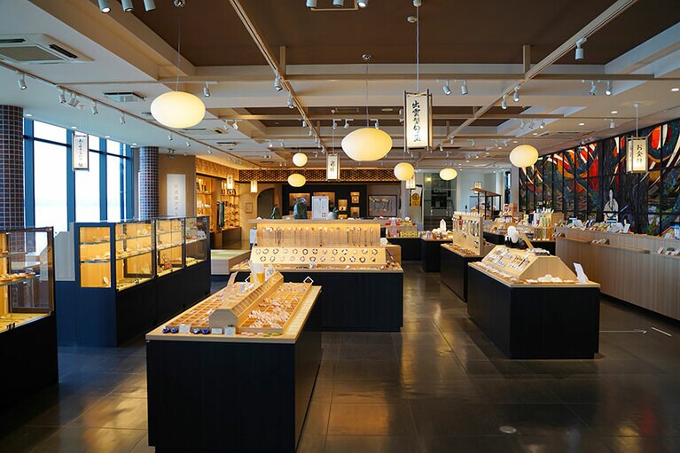 神秘的な光を放つメノウのアクセサリーや、まがたまアイテムが所狭しと並ぶ。制作風景が見学できる工房や食事処も併設。