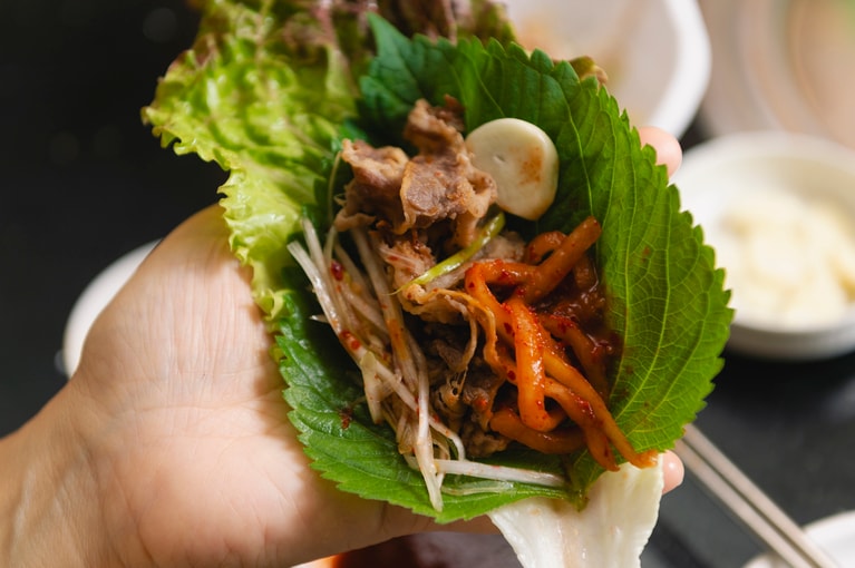 サンチュやエゴマの葉に肉をのせ、ネギサラダや大根サラダ、ニンニク、お好みの野菜を包めば完成！