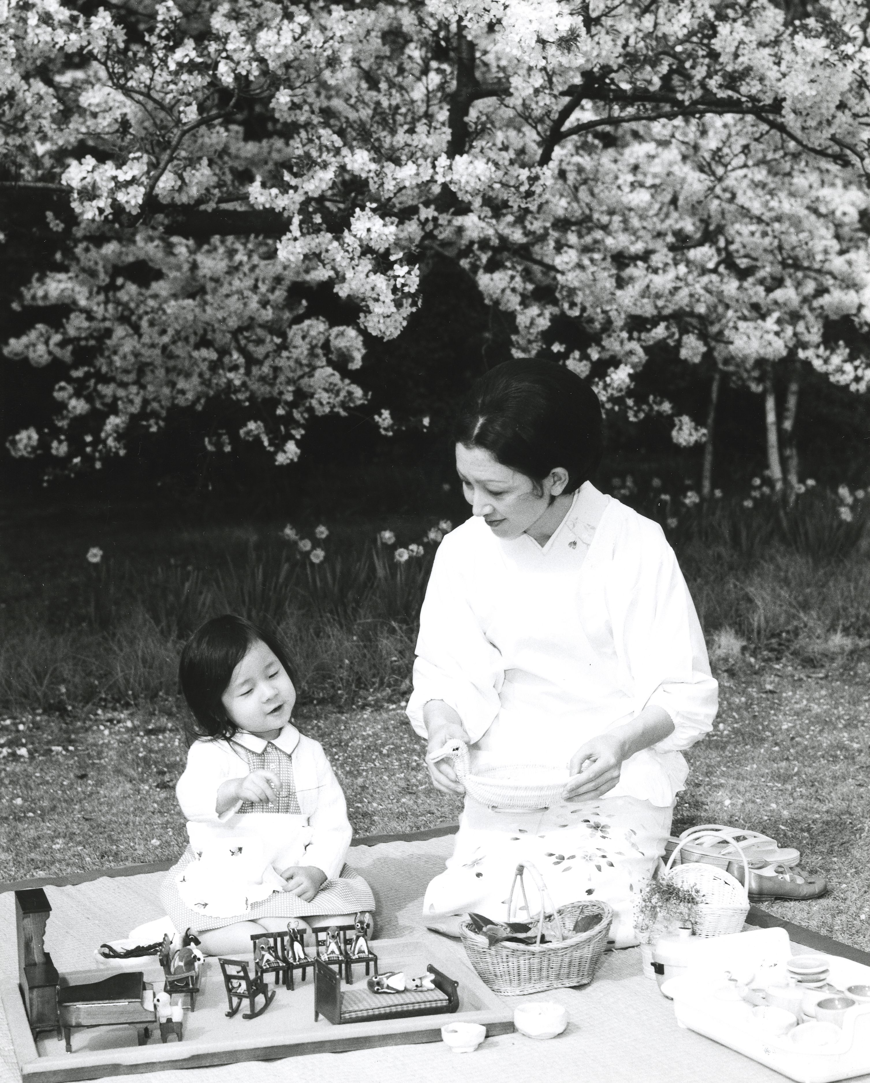 桜の花びらが散る東宮御所のお庭で、美智子さまとおままごと。ミニチュア家具の上に並ぶのは小さな犬の人形　宮内庁提供