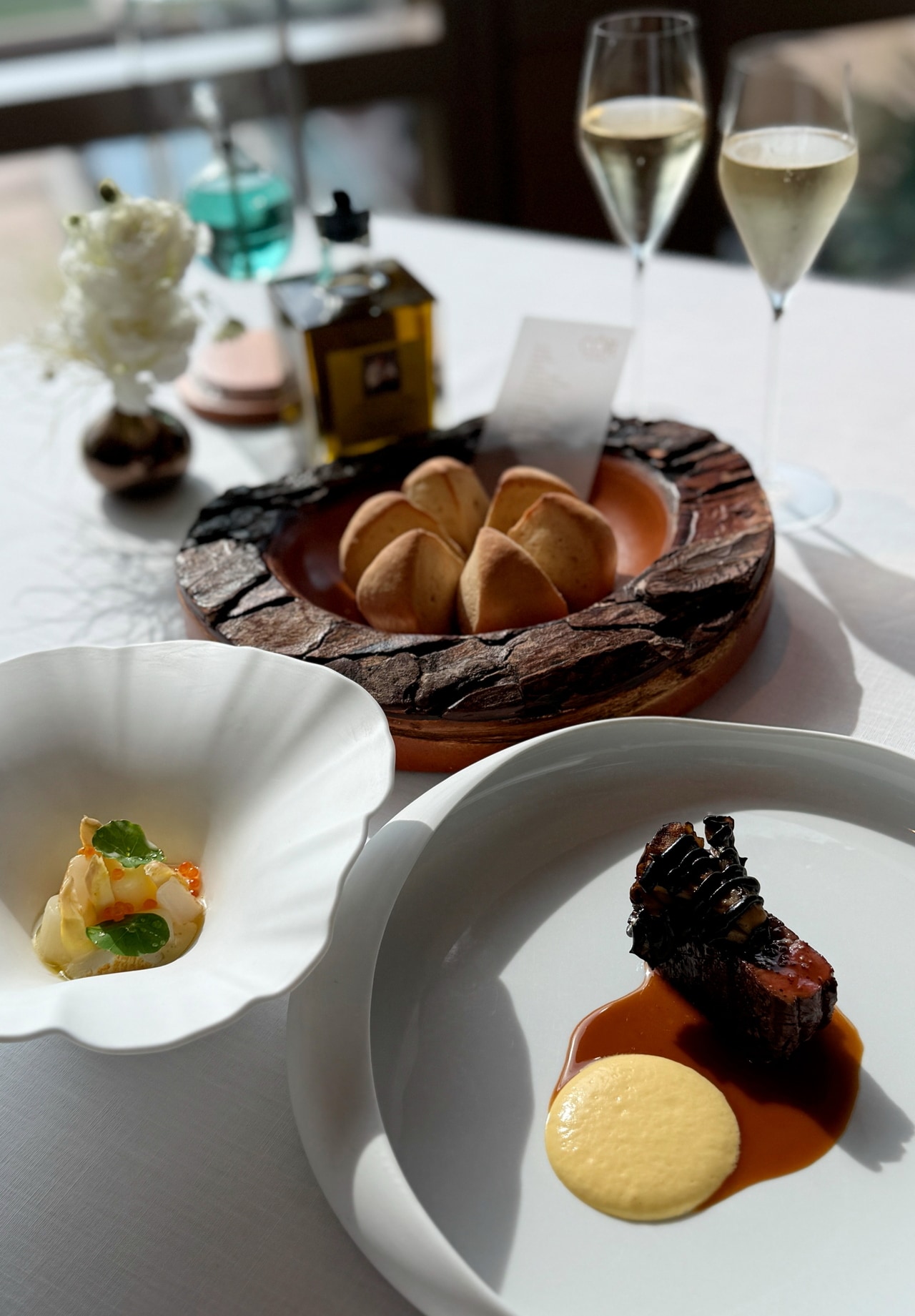 「コート バイ マウロ・コラグレコ」の料理。手前右は、牛ヒレ肉に舞茸とグリーンペッパーを合わせた一皿。手前左は、スラーターニー産コウイカとホワイトアスパラガス。中央の「パン・ド・パルタージュ」は、コラグレコシェフが祖母から受け継いだレシピで作った、この店のスペシャリテ。マントン産レモンで香りづけした特製オリーブオイルとともに。