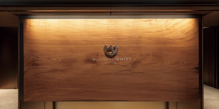 エントランス正面では樹齢約1,000年の欅の一枚板が出迎えてくれる。シンボルマークは鋳物で造られ、「IMPERIAL HOTEL KYOTO」の文字には螺鈿細工が施してある。