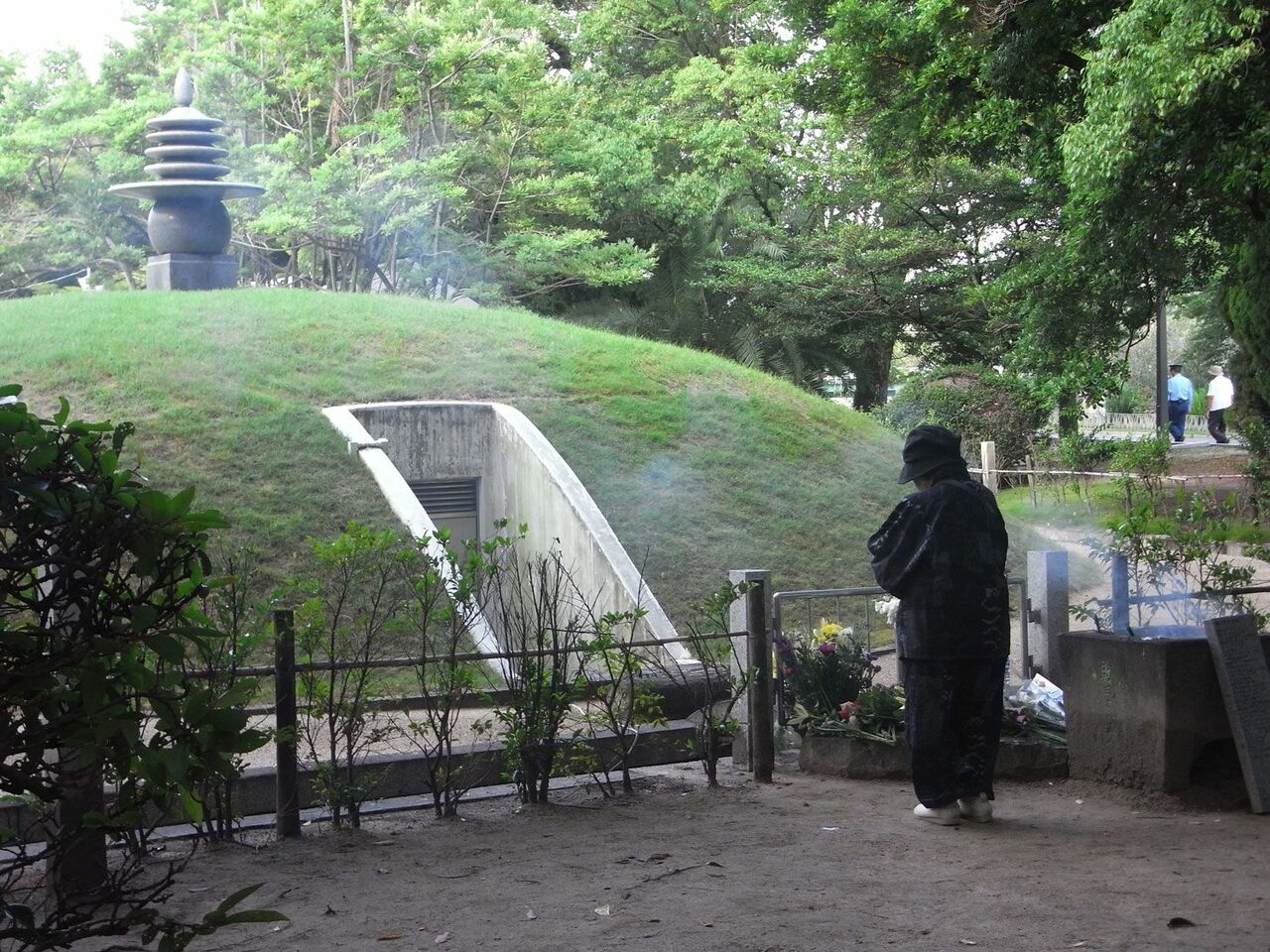 原爆供養塔の北側。地下の納骨堂に下りていく入り口が見える。ご遺族が、納骨堂に向かって手をあわせている。 写真：堀川惠子