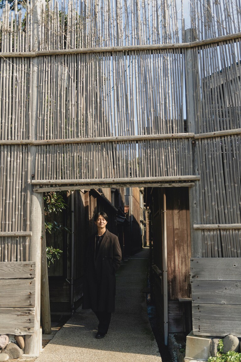 集落入口に立つ竹囲いの前で。宿根木には当時の町並みがそのまま残り、時代を超えた空気感を味わうことができる。