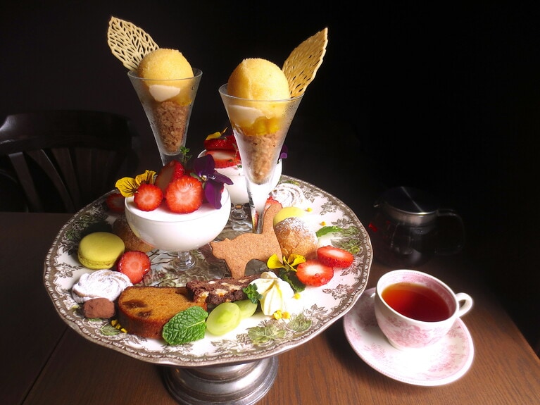 「デザートプレート」1,870円（スタンドは2人前）。紅茶880円。取材時は、奈良県のいちご「古都華」を使用。スペイン産オレンジを使ったスターアニスのソルベ、パイナップルのコンフィチュール、イチジクとキャラメルのパウンドケーキ、チョコとくるみのカントゥッチ、ネコのスペキュロス（ベルギーのお菓子）、パッションフルーツのギモーヴ、キャラメルクリームのプチシュー、アーモンドチョコレート、マカロン、黒糖のバタークッキー、メレンゲ、自家栽培のハーブ。