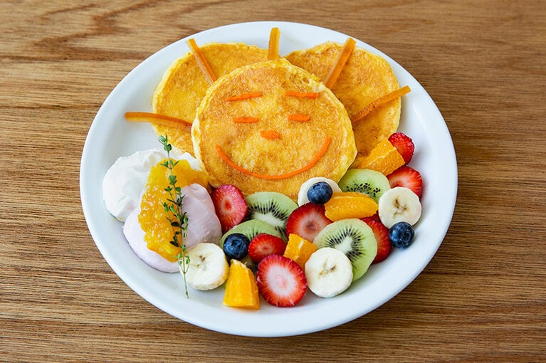 あおむしが生まれた朝の“おひさま”をフレンチトースト風パンケーキで表現した、おひさまパンケーキ 1,700円。暖かな表情の太陽のもと、たっぷりのフルーツを食べて成長する冒頭シーンが一皿の中に描かれている。