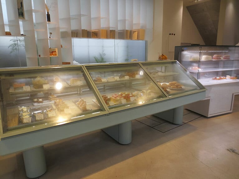 正面に生ケーキのショウケース。右手にカヌレ、道路側にクッキーが並ぶ店内。