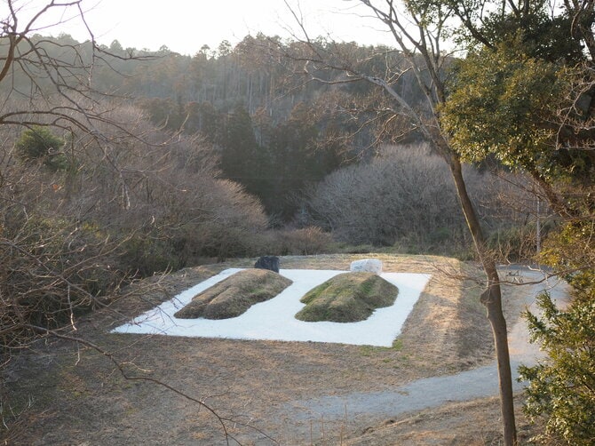那覇市を拠点に世界各地で活動する島袋道浩の作品。春夏は ”カラダ”から草花が繁茂する様子が、秋冬に向けて枯れていく姿など、四季折々の変化を楽しむことができる。 島袋道浩《ツチオとツチコ：55年後のBED PEACE》 【左側の体】北海道の石、市原市、君津市、袖ケ浦市、富津市の土 【右側の体】沖縄の石、クルックフィールズの土 【ベッド部分】白砂利 ／2024年