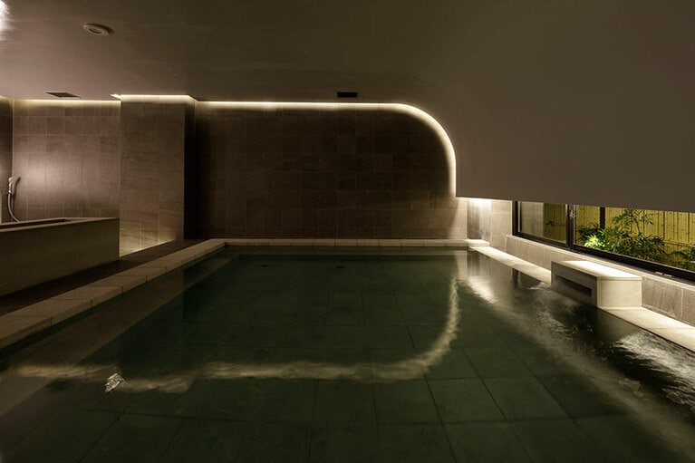 湯船には石川県で採れる滝ヶ原石を使用。ゆるやかな曲線の天井に包み込まれるような空間で、旅の疲れを癒せる。(photo：志摩大輔)