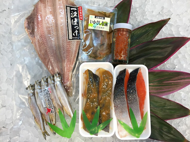 おためしセット 7,300円。左上から時計回りに：特大シマホッケ 1枚、いかさし松前漬け 120g、正油いくら 50g(瓶入り)、北洋産紅鮭 2切れ、銀だらみそ漬け 2切、本シシャモ(オス) 5尾／丸宇中村商店