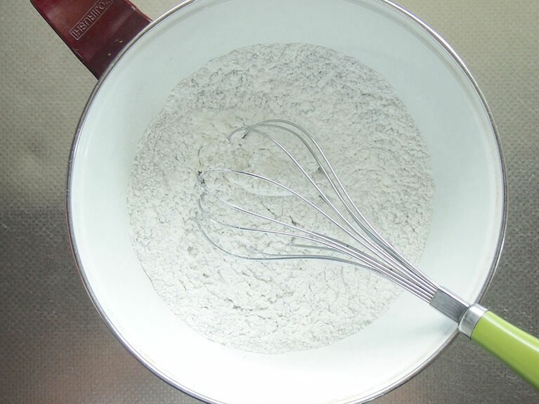 (1) 黒炒りごまは、すり鉢ですり潰します。ボウルに米粉、黒ごま、ベーキングパウダー、きび糖を入れて泡立て器を使ってよく混ぜます。