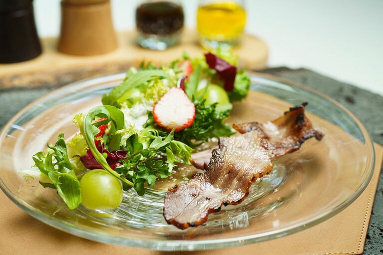 旬のフルーツを加えたサラダに、藁の香りをまとわせた猪のベーコンを添えて。