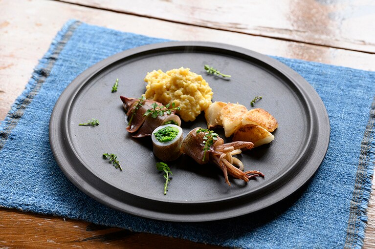 昼の「蕎麦懐石 B」4,000円より。876 pottery（陶工房 弥七郎）の器で供された「ヤリイカのさっと煮」は、あご（飛び魚）だしの蕎麦つゆで炊いた菜の花をヤリイカに詰め、カツオだしの蕎麦つゆで炊いたもの。添えられているのは、ソースとしても味わえるトロトロに固めた炒り卵と香ばしくソテーしたカブ。