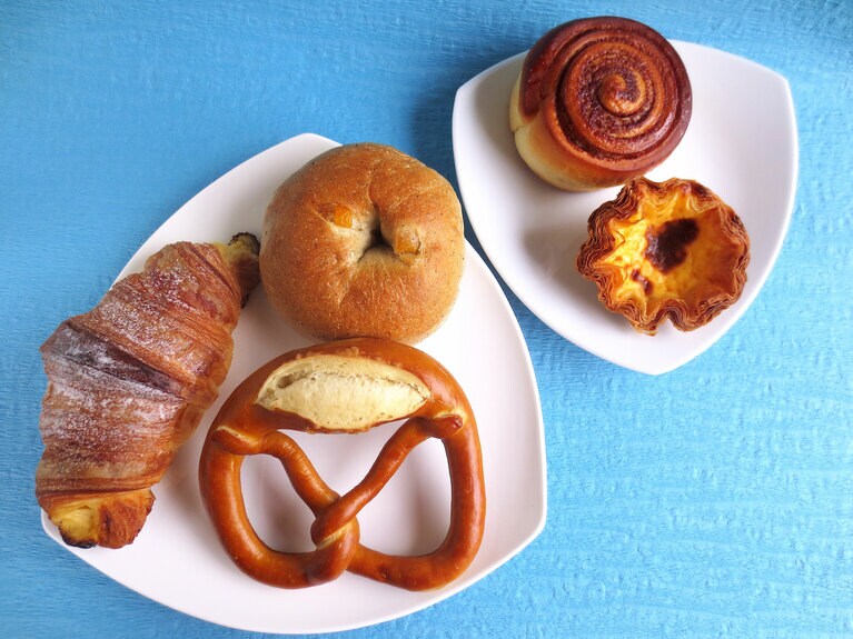 世界各国のパン。左の器の左より時計回りに「イタリアンクロワッサン」280円、「台南マンゴークリームチーズベーグル」280円、「プレッツェル」180円、右の器の上「シナモンロール」220円、「エッグタルト」380円。