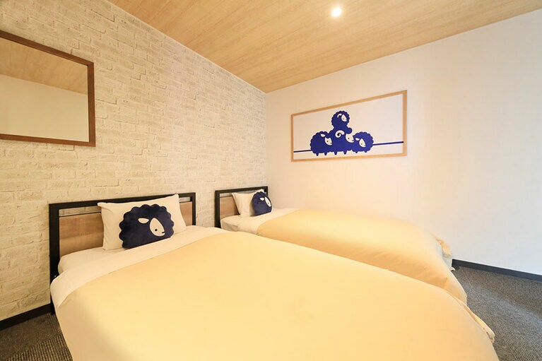 洋室ツインの客室。枕などにイメージキャラクターの羊のロゴがあしらわれている。