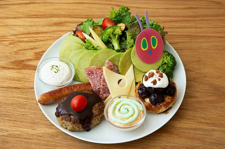 あおむしが成長する過程で食べる印象的な食材が一皿に凝縮された、はらぺこあおむしパンケーキ 2,300円。ほうれん草のパンケーキで表現された“はらぺこあおむし”を中心に、ソーセージやチーズ、チョコレートケーキに見立てたハンバーグ、アイスクリームに見立てたタラモサラダなどが並ぶ。子供と一緒にシェアするのもオススメ。