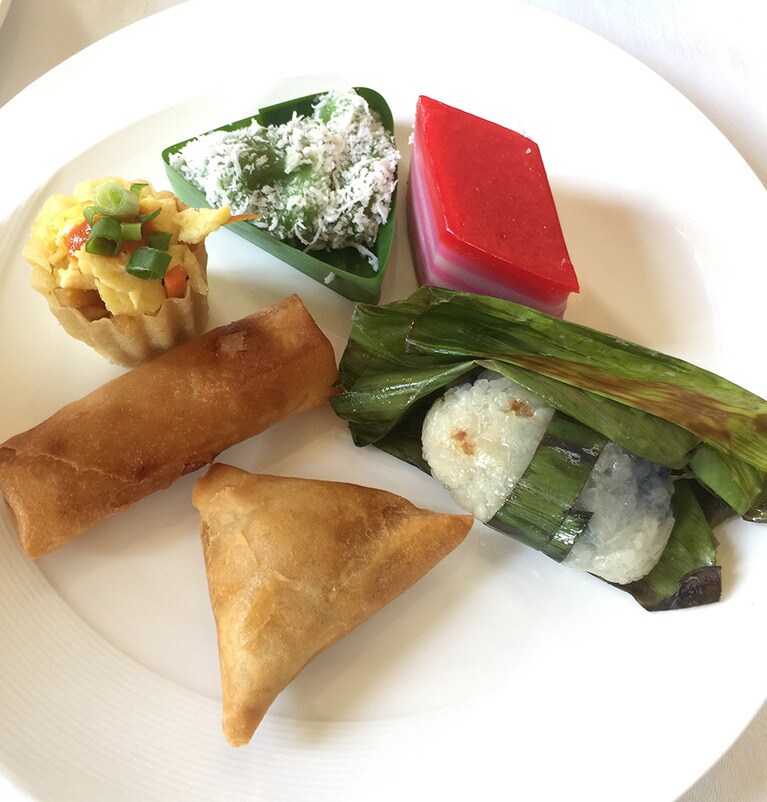 手前より時計回りに、カレー味の三角サモサ、春巻、名物の前菜「トップハット」。葉っぱの三角の箱に入ったものは、ココナッツをまぶした餅「オンデ・オンデ」、しましま模様の伝統菓子「クエ・ラピス」、餅米の「プルッ・ウダン」。