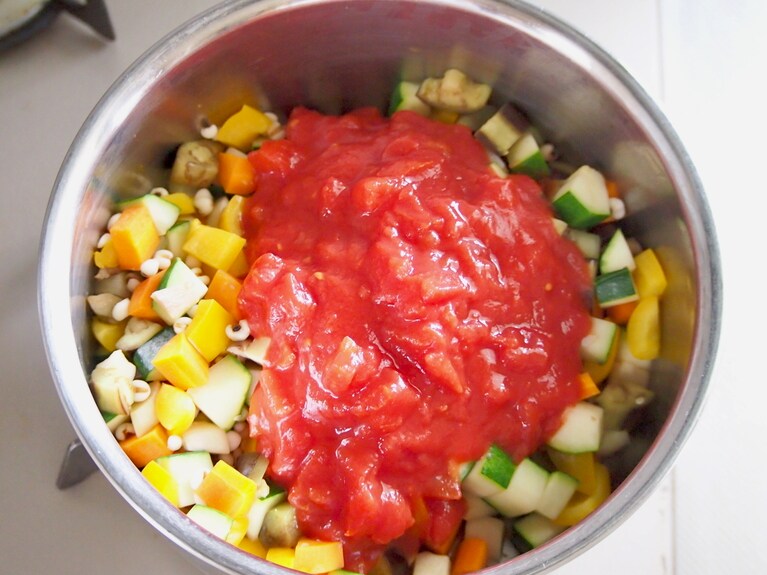 ゆっくり弱火で炒め、野菜全体にオイルが絡まったら、トマト缶を入れる。全体を混ぜ合わせ、弱火で煮込む。