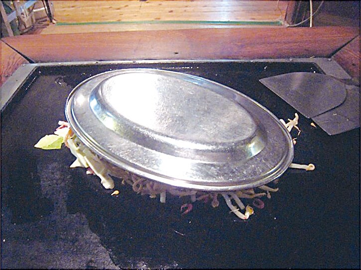 皿を被せて蒸し焼きにする（2012年撮影）。