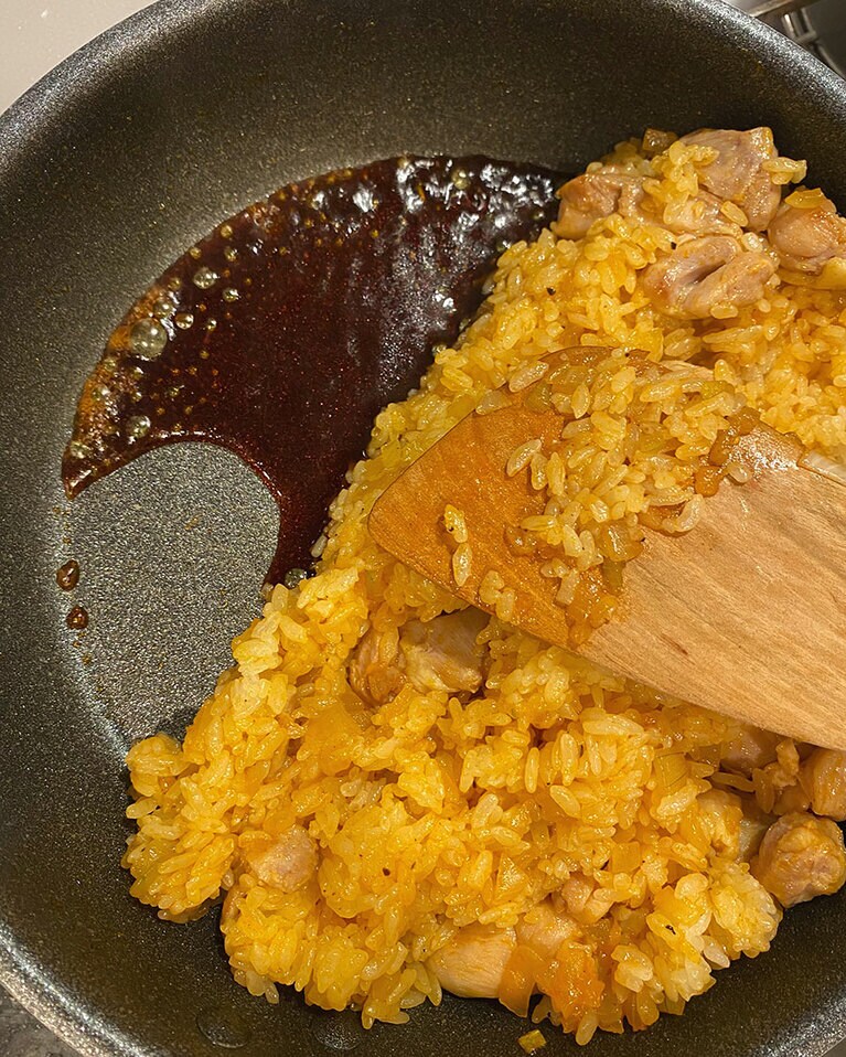 【焦がし醤油のケチャップライスが主役のオムライス】(6) ごはんを端に寄せ、少し火力を上げる。空いたスペースに【A】を一気に加えてふつふつとしてきたら、満遍なくごはんと混ぜ合わせて火を止める。