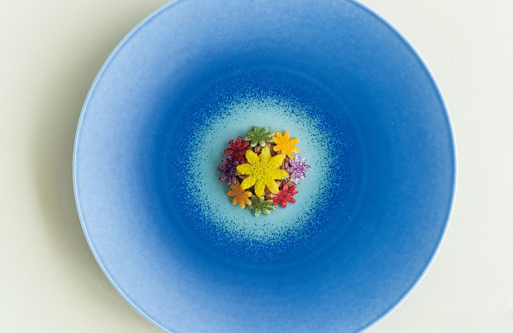 古宇利島で独創的な料理を提供する「6Six(シス)」。“ホタルイカのバジル酢味噌”は、花形にカットした大根を、ビーツや菊、赤きゃべつなどのパウダーで色付けし、まるでお花畑のように華やかな一皿だ。